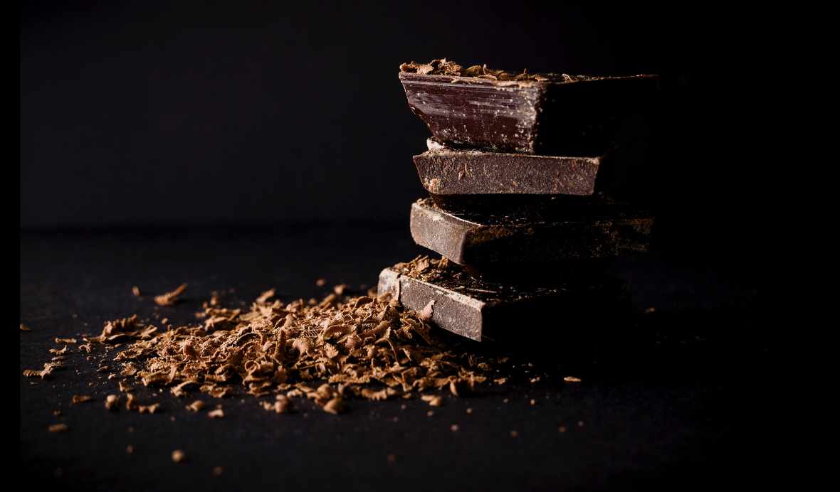 aesthetic photograph of a stack of dark chocolate bars next to a layer of ground up cocoa powder